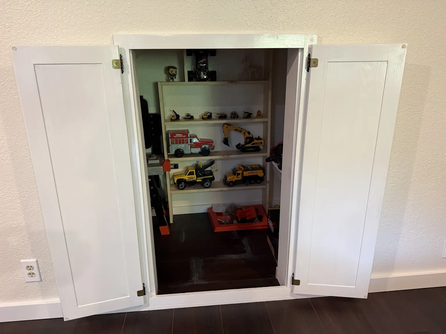 Open double doors revealing shelves of toy trucks and a compact children's play and storage nook